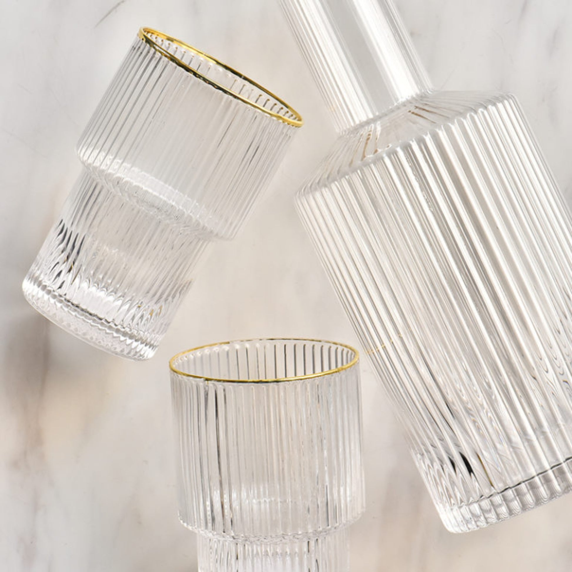 The larger size set of the Izmir gold ripple glass carafe and two glasses on a white table to highlight the gold rim from another view