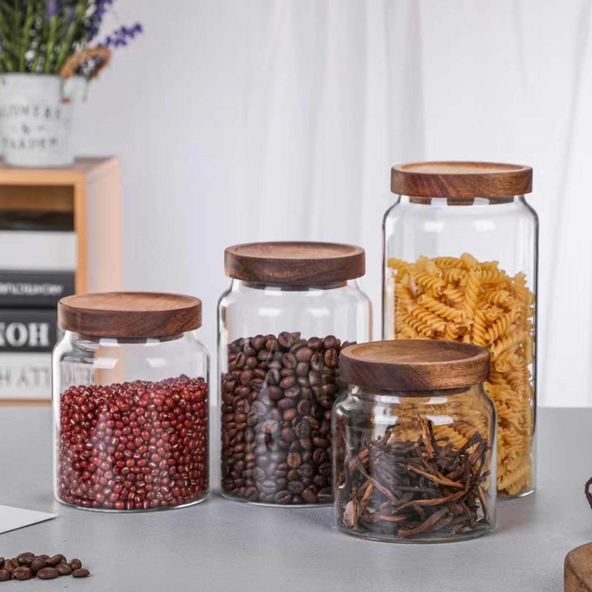 Four different size glass jars with acacia lids containing pasta, coffee and beans in them
